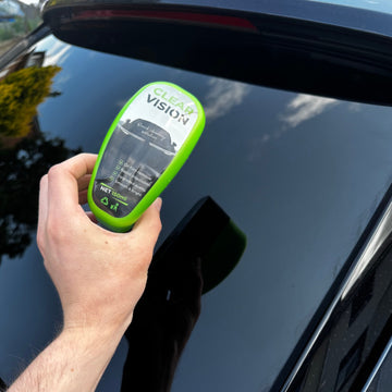 Hand holding a ClearVision Glass Cleaner bottle against a black car window