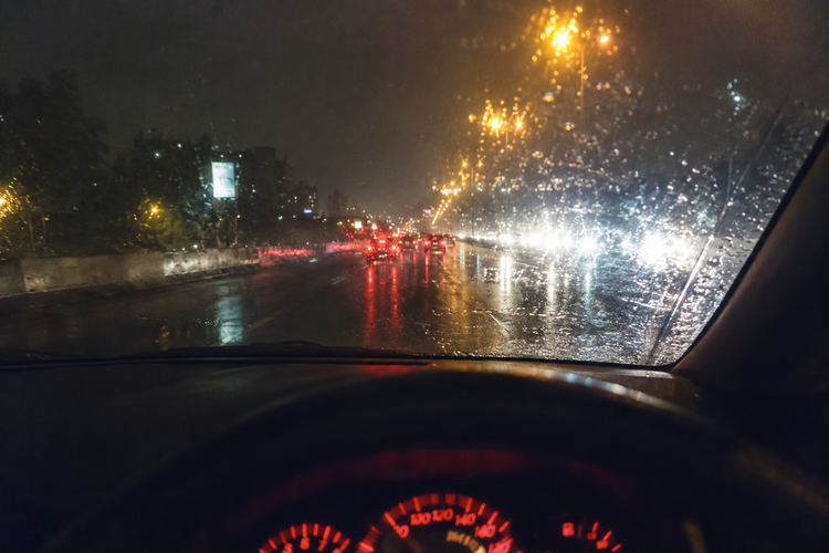 Raindrops on a car windshield at night with city street lights and car headlights in the background