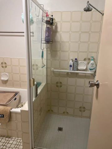 Shower stall with beige tiled walls, a shower head, and soap dispensers on a shelf.